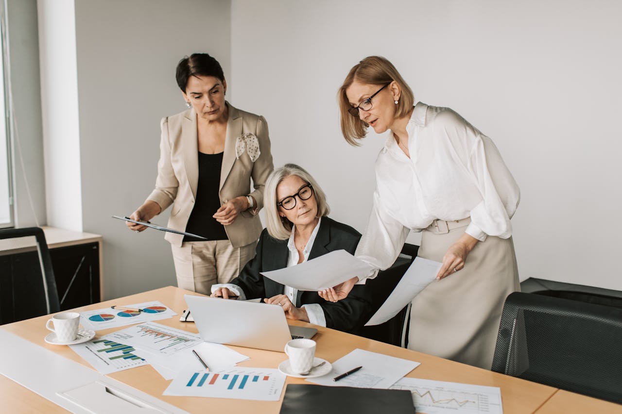 home-hero Three businesswomen discussing reports in a modern office environment.